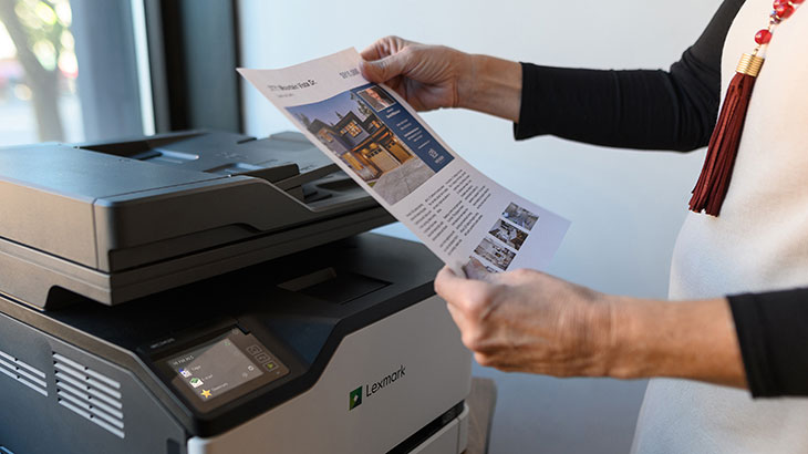 Woman holding color printed brochure near Lexmark printer