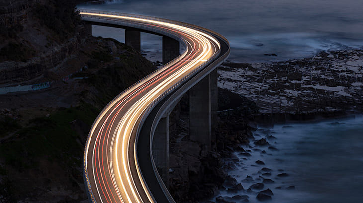 Lights blurring around a corner on a bridge at dusk