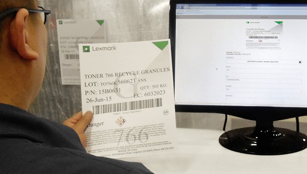 Lexmark employee sitting at computer holding old manufacturing hazardous label in order to make a new one on the computer screen.